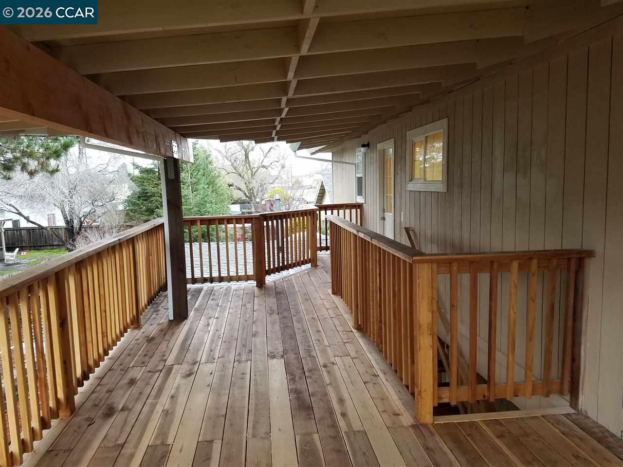 Covered wooden deck with plank flooring and railings beside the house.