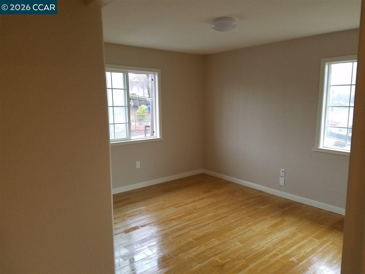 Empty room with polished hardwood floors and two windows.