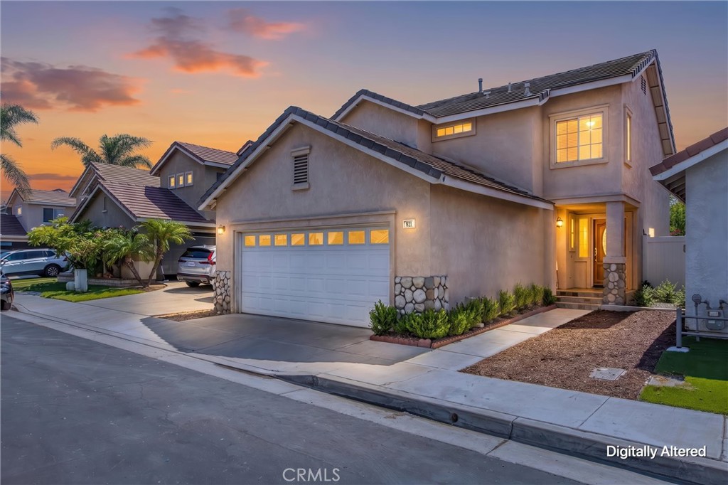 Two-story stucco home with a double garage and illuminated entry at dusk.