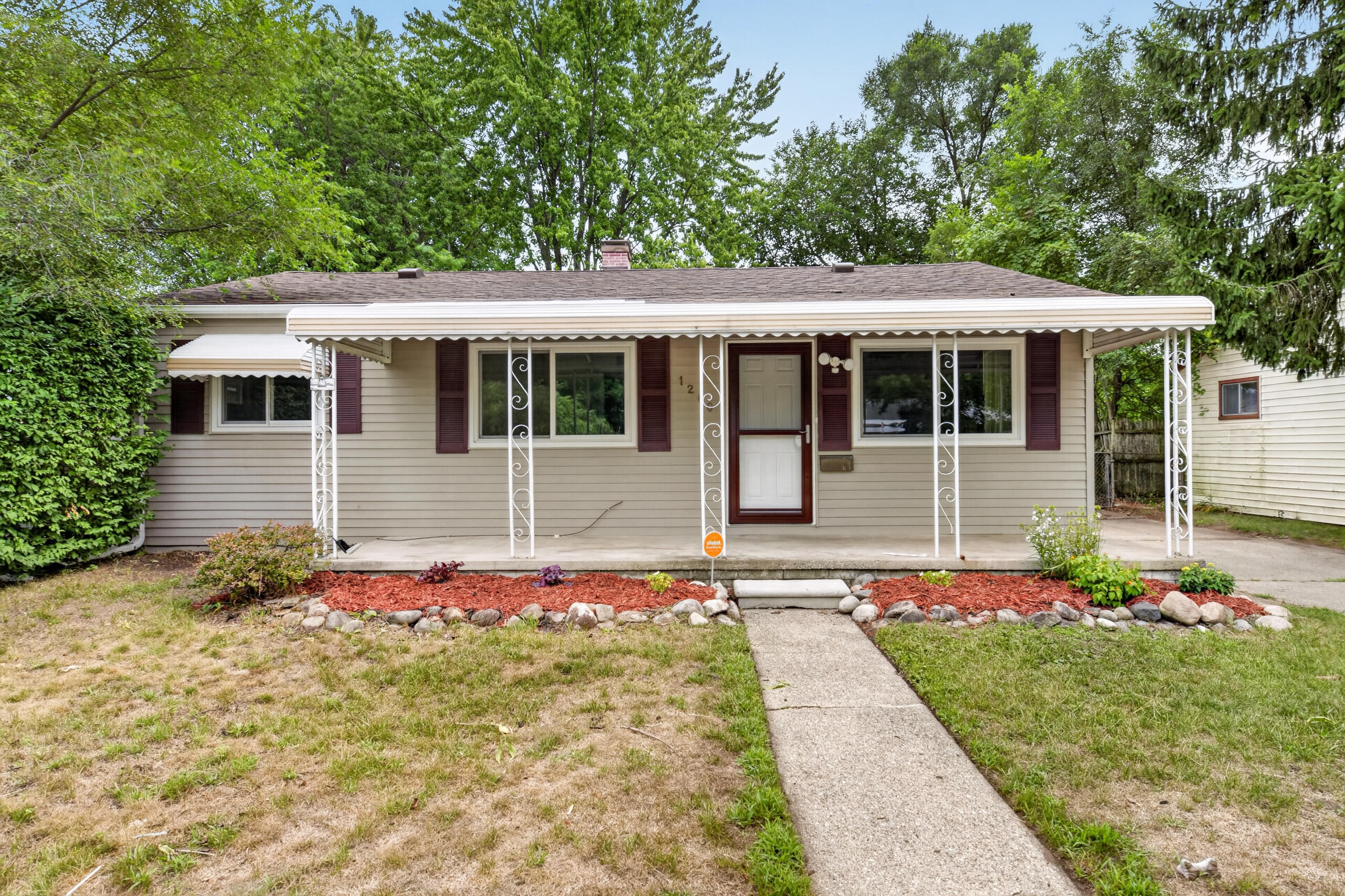 Single-story beige house with burgundy shutters, a covered porch, and a walkway through the front yard.