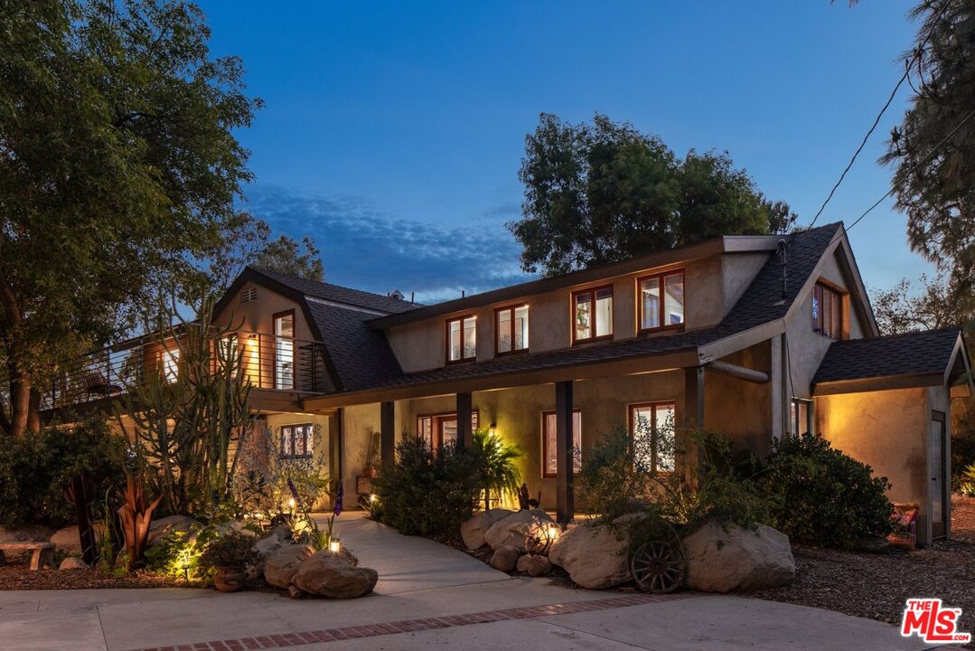 Two-story stucco home at dusk with a covered porch and warmly lit windows.