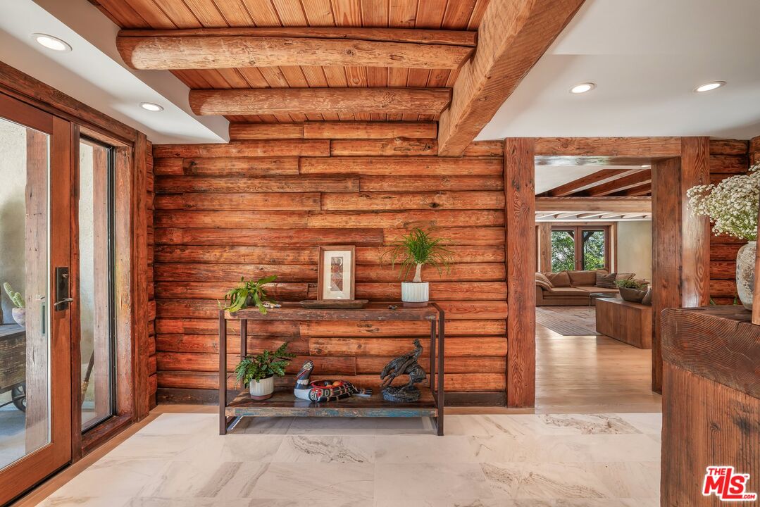 Wood-paneled entry foyer with exposed beams, a console table, and an opening to the living room.