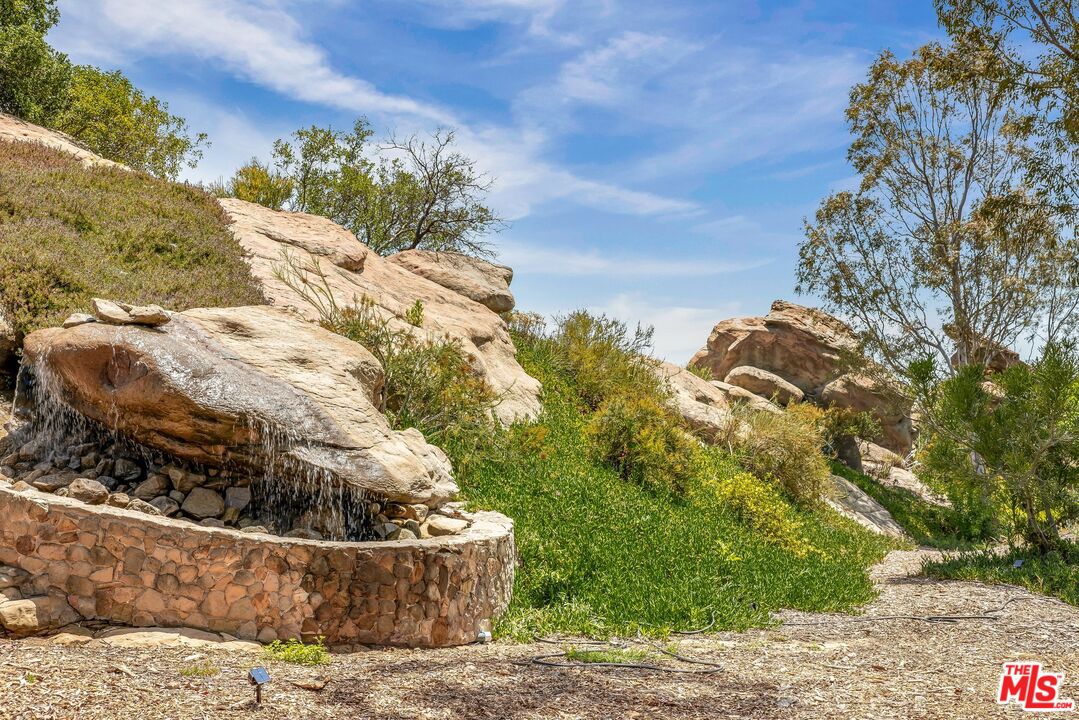 Landscaped yard with a stone waterfall feature among large boulders and shrubs.