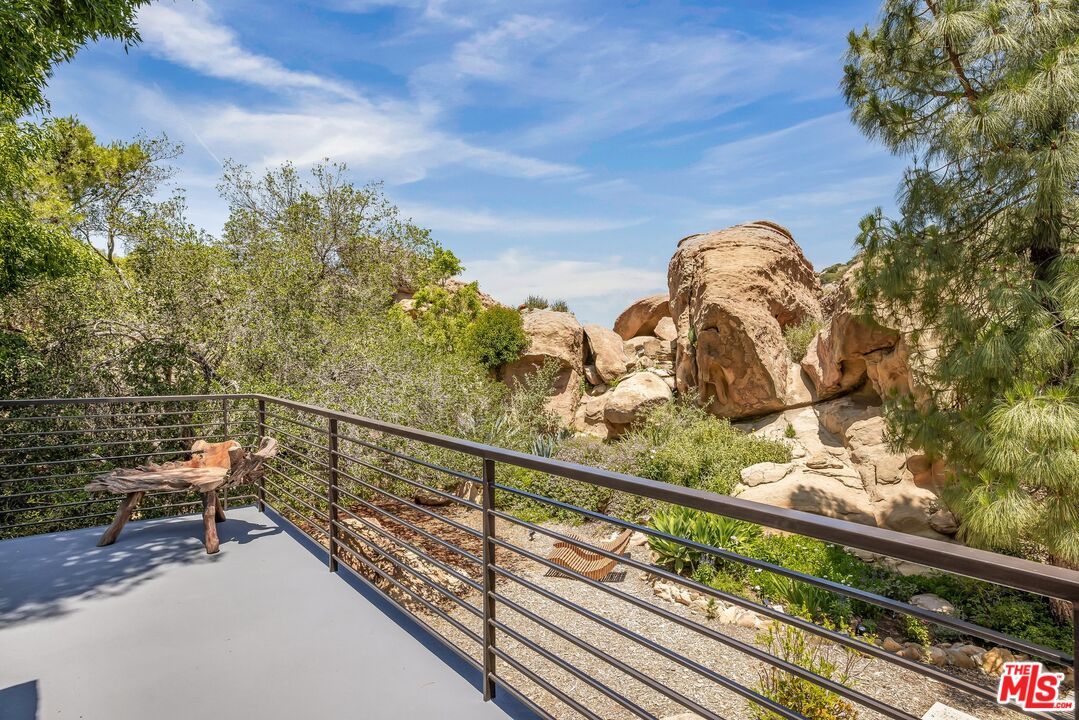Patio with black railing overlooks a landscaped yard and dramatic tan rock formations.