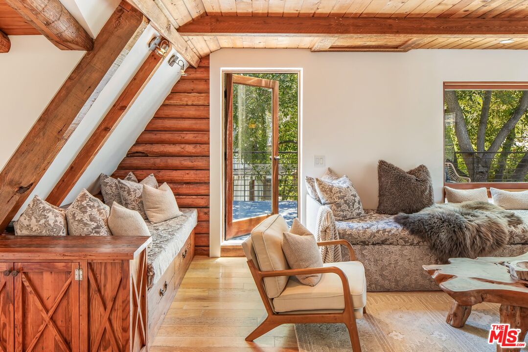 Living room with exposed timber beams, built-in window seating, and large windows overlooking trees.