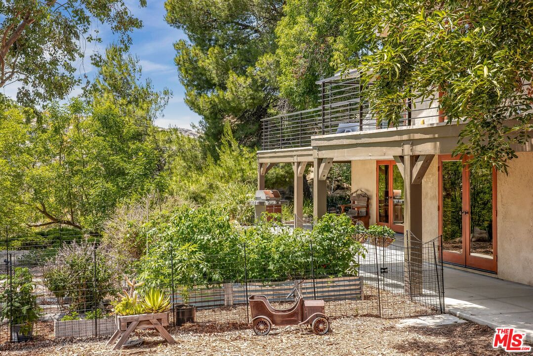 Backyard with a raised deck, fenced garden, raised planters, and barbecue beside French doors.