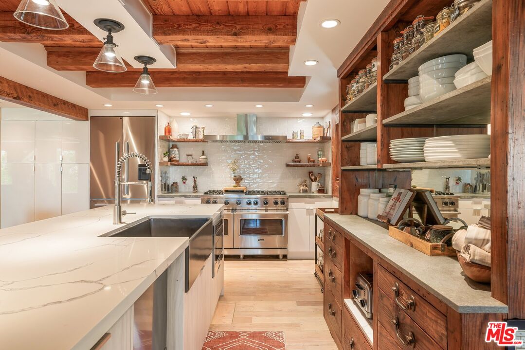 Kitchen with a white veined island, stainless range, and exposed wood ceiling beams.