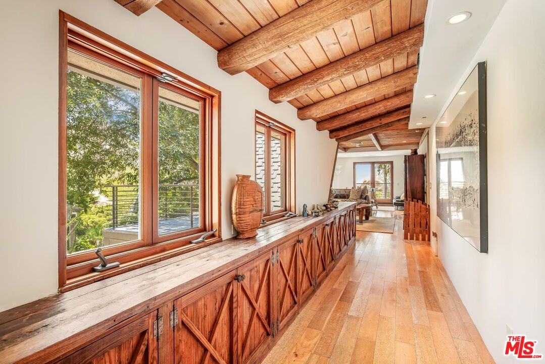 Hallway with exposed timber beams, rustic wood cabinetry, hardwood floors, and large windows.