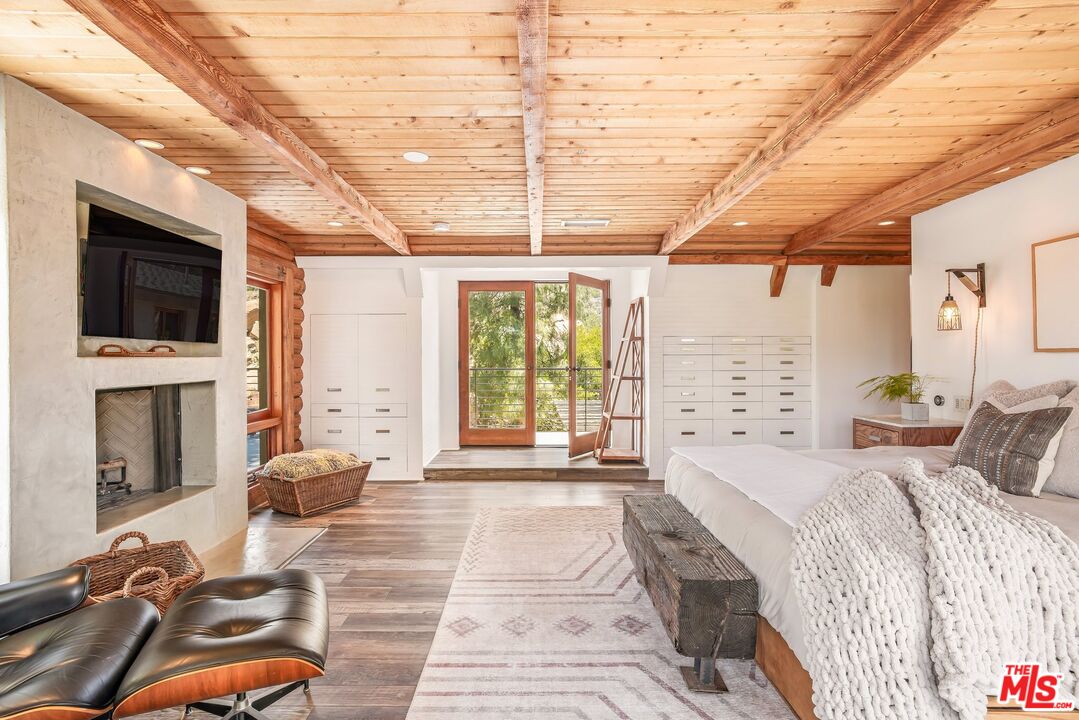 Bedroom with a wood-plank ceiling, fireplace, built-in drawers, and glass doors opening to trees.