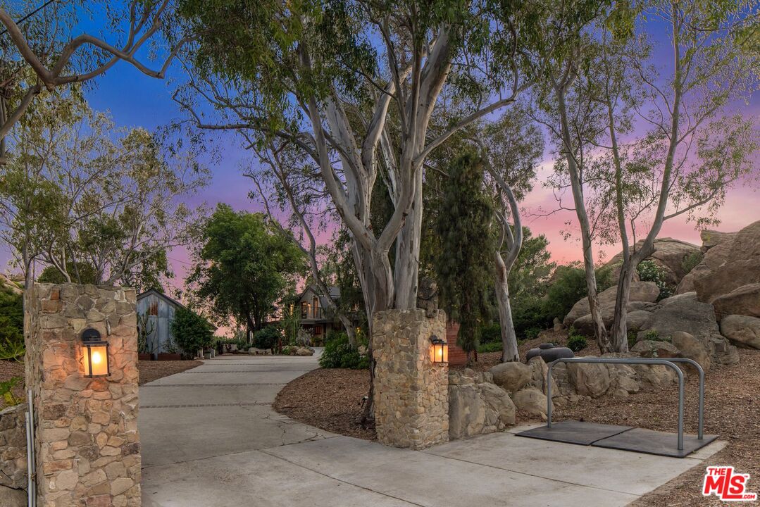 Stone-pillared driveway entrance beneath mature trees at dusk.