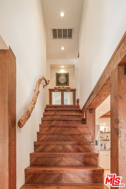Rustic wooden staircase with patterned treads, a branch handrail, and a round mirror on the upper landing.
