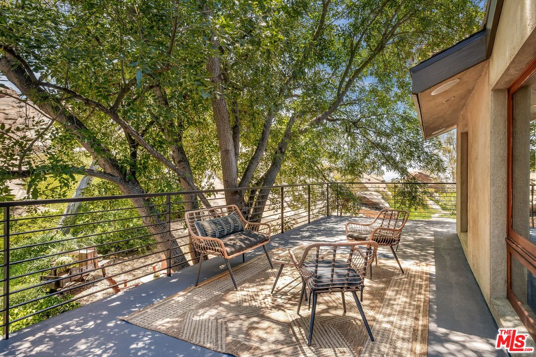 Patio with woven lounge chairs and a rug beneath a leafy tree canopy.