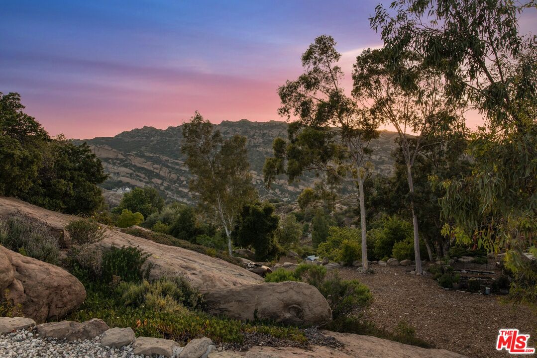 Rocky landscaped hillside overlooking rugged mountains beneath a pink sunset sky.