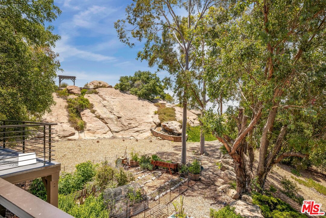Rocky landscaped backyard with mature trees, raised planters, gravel paths, and a deck with metal railing.
