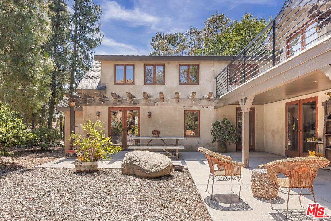 Two-story home with a pergola-covered patio, balcony, and wicker seating in a wooded backyard.
