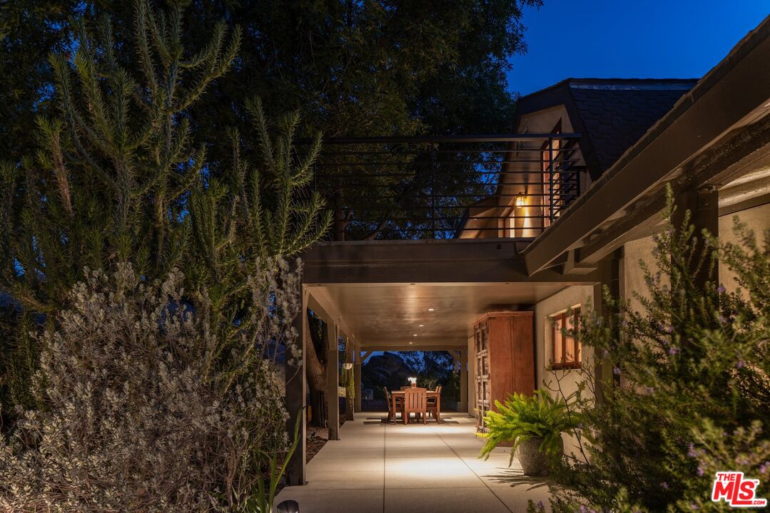 House exterior at dusk with a covered dining patio, upper deck, and mature landscaping.