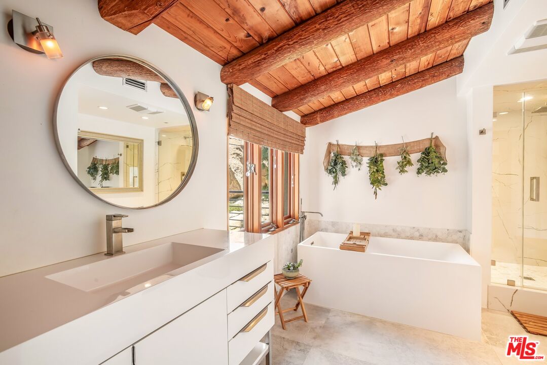 Bright bathroom with a soaking tub, glass shower, double vanity, and exposed wood ceiling beams.