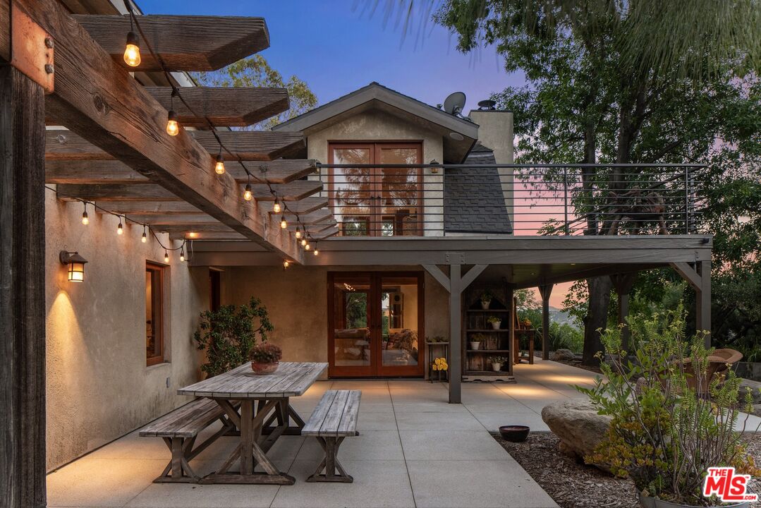 Rear patio with a raised deck, pergola string lights, and a wooden picnic table at dusk.