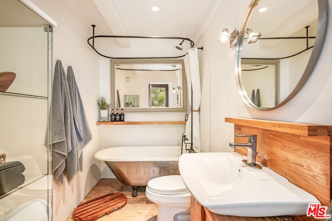 Bathroom with a freestanding copper-toned tub, wood vanity, and glass-enclosed shower.