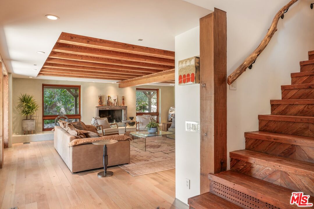 Living room with exposed wood beams, a fireplace, and a rustic timber staircase.