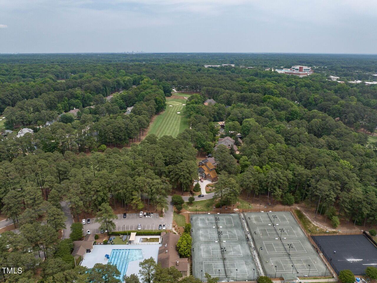 Aerial view of a wooded community with a golf course, pool, and tennis courts.
