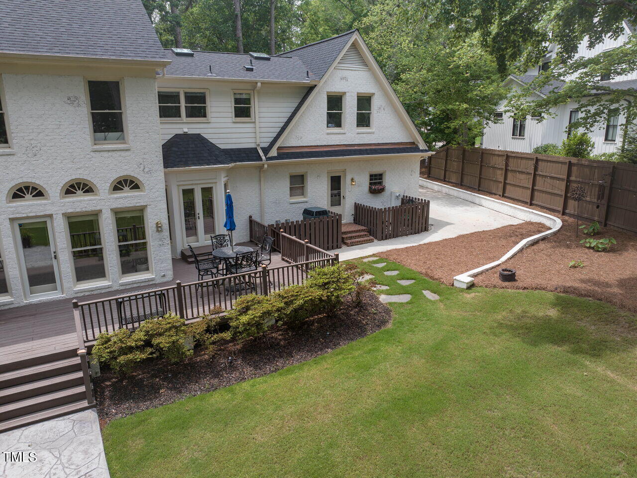 White two-story home with a raised deck, fenced patio, and broad lawn.