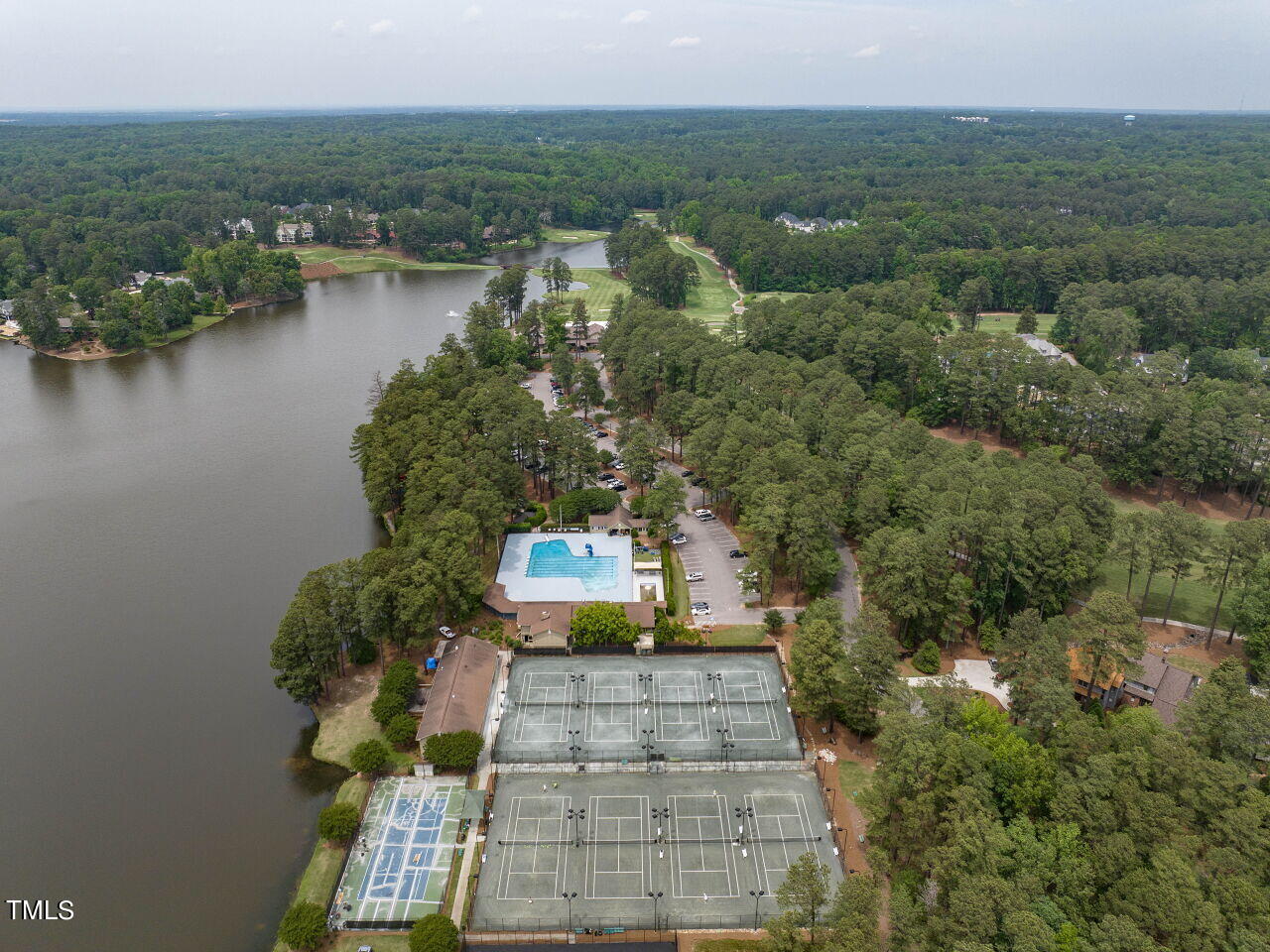Aerial view of a wooded lakeside community with tennis courts and a swimming pool.