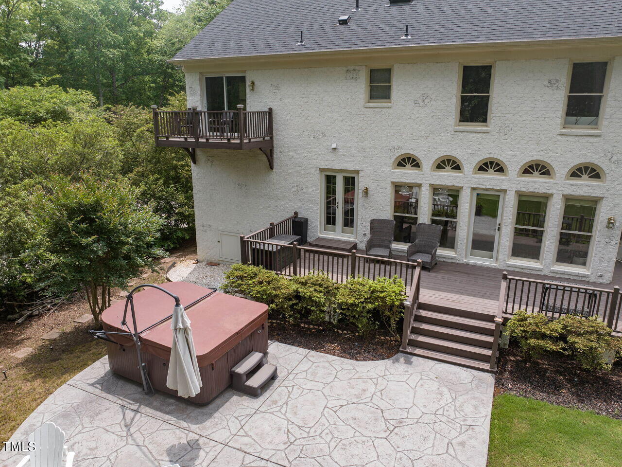 Rear of a white brick house with tiered decks, a stone patio, and a hot tub.