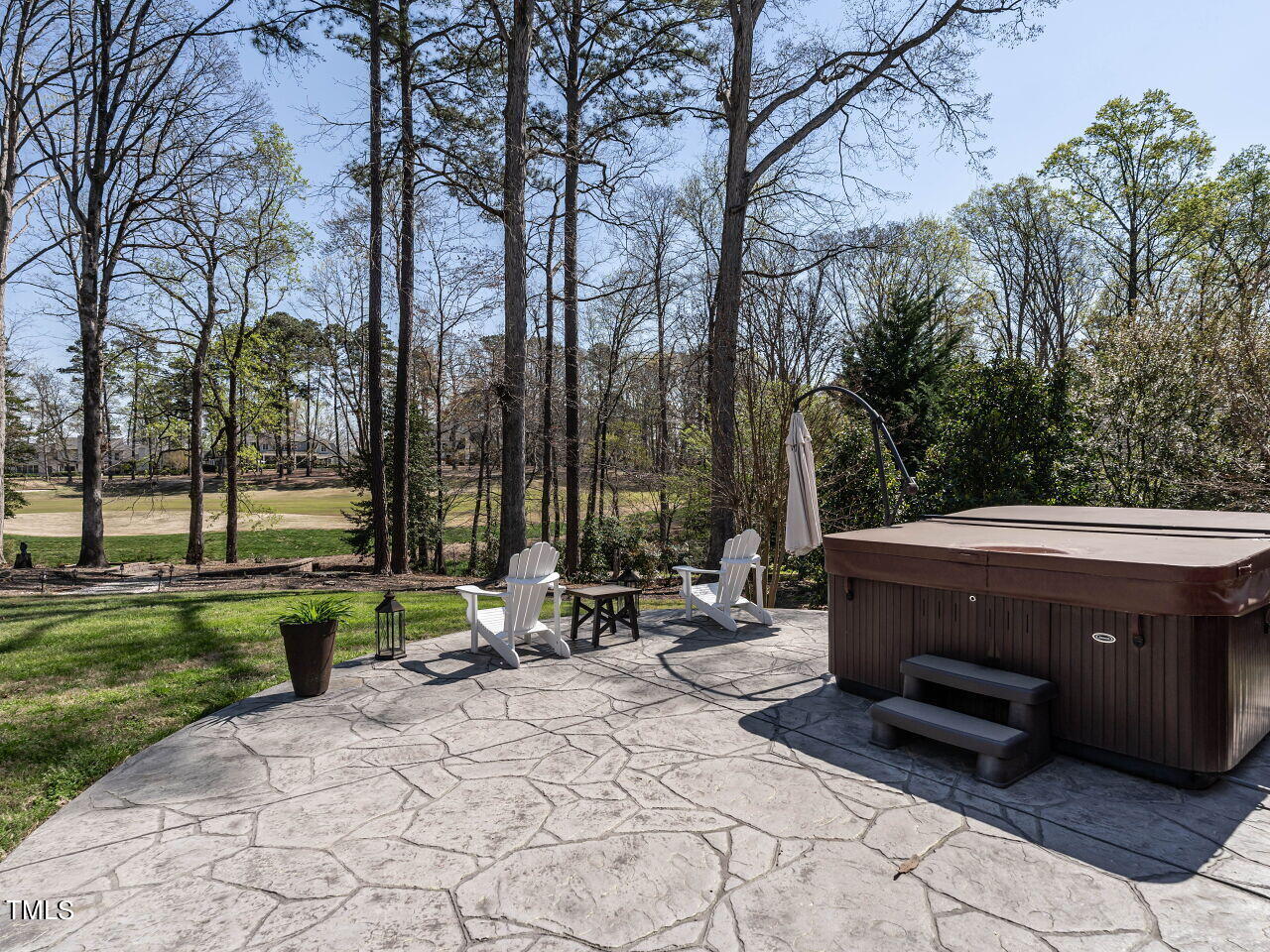 Backyard patio with a hot tub, Adirondack chairs, and a wooded lawn.
