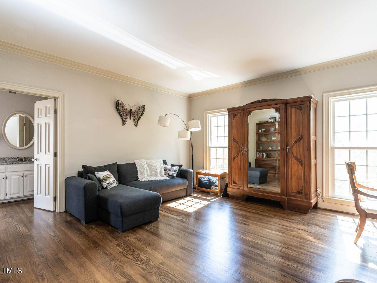 Living room with a charcoal sectional, carved wooden cabinet, and sunlit hardwood floors.