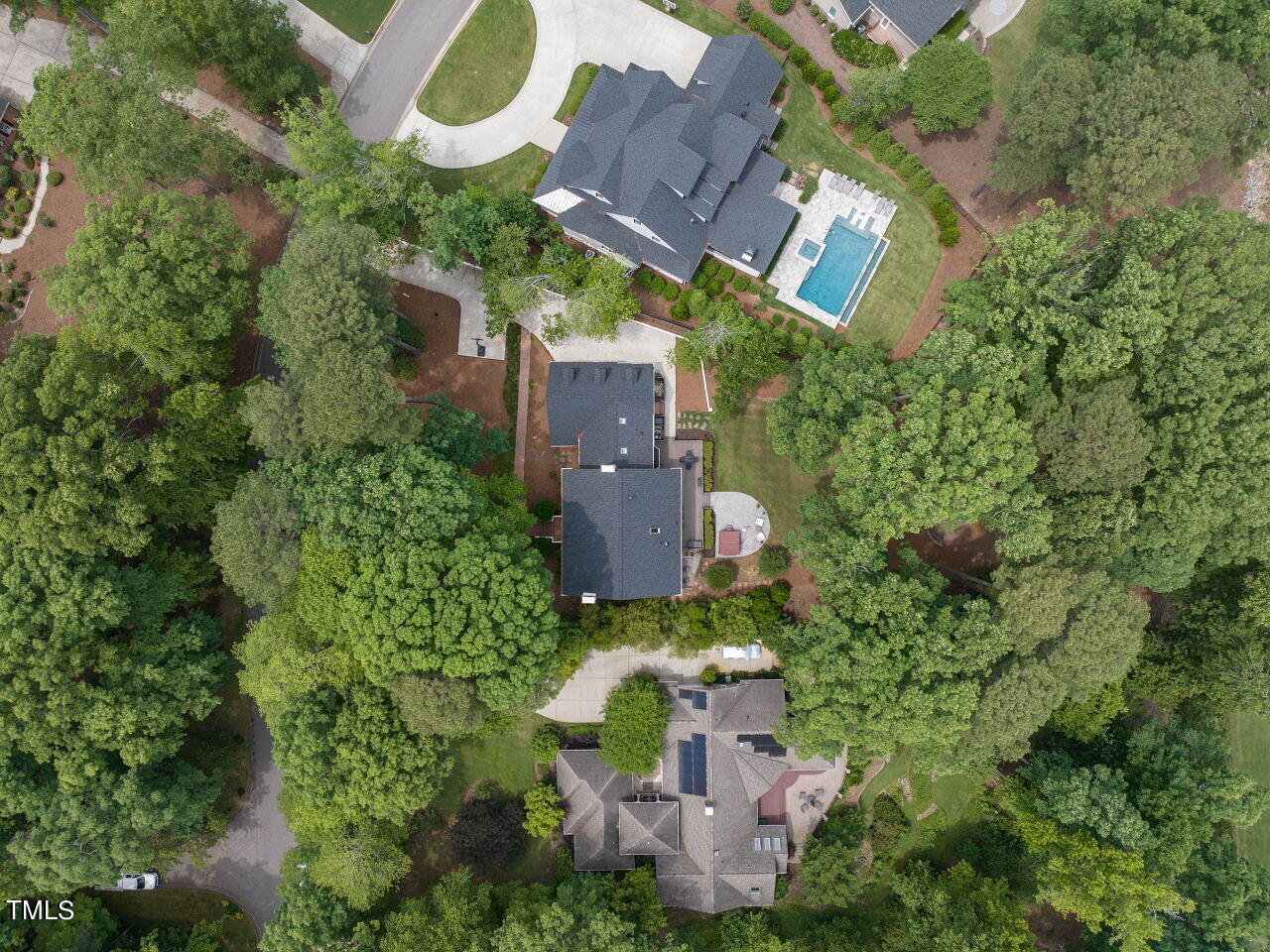 Aerial view of a tree-surrounded home with a broad driveway and landscaped yard.