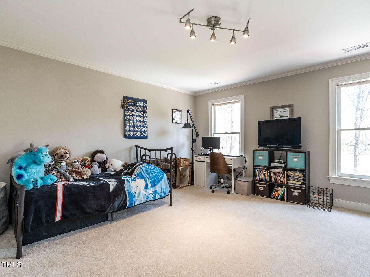 Bedroom with a single bed, plush toys, desk, and television between two windows.
