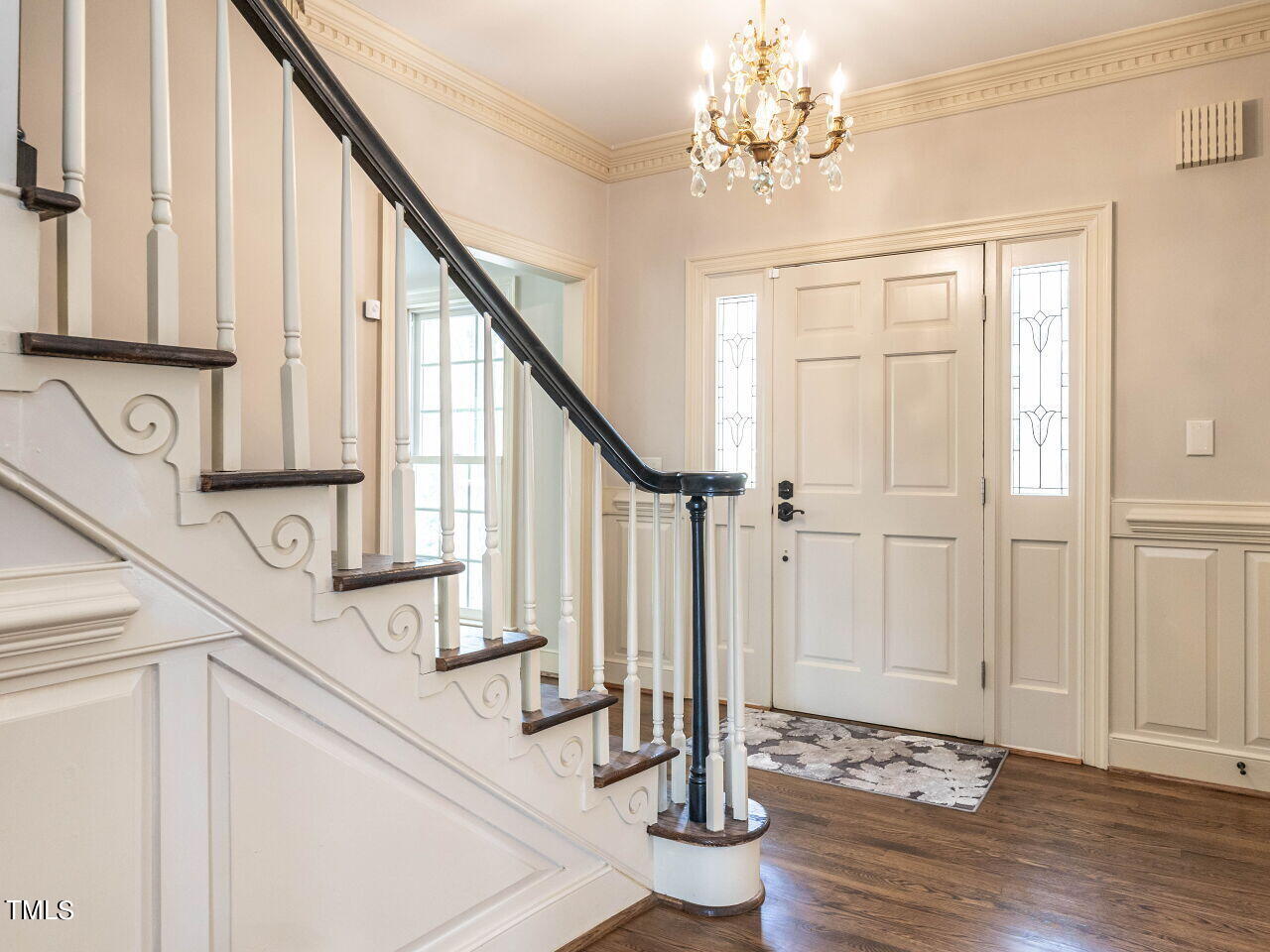 Foyer with a decorative staircase, crystal chandelier, and paneled front door with glass sidelights.