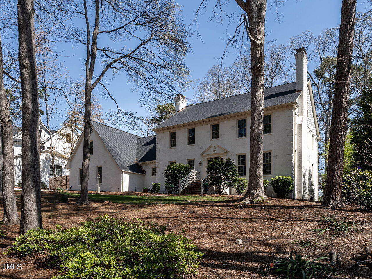 Two-story white house with front steps, framed by tall trees and a landscaped yard.