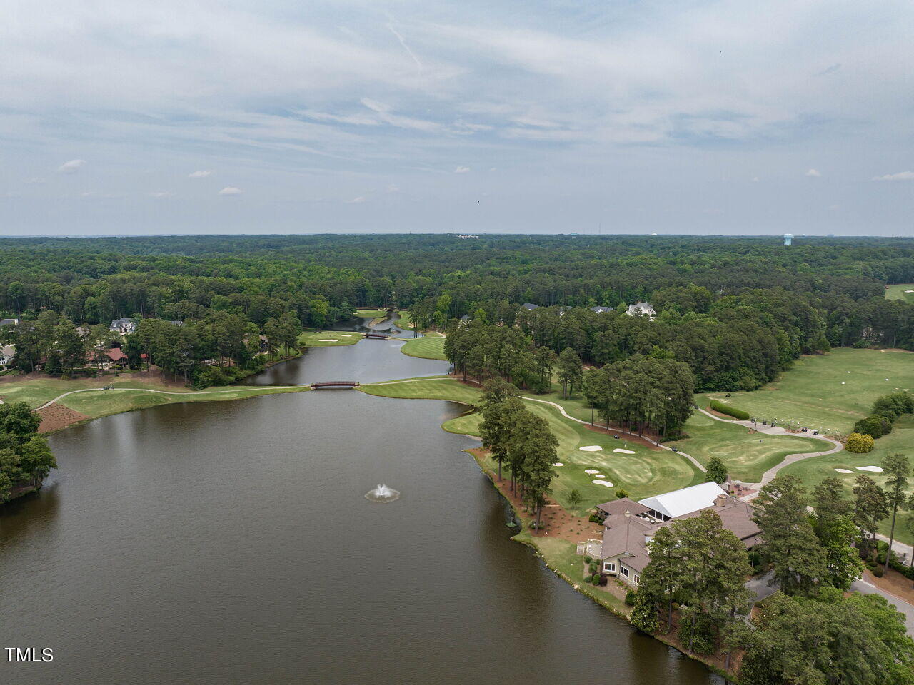 Aerial view of a lake and golf course bordered by homes and dense woodland.