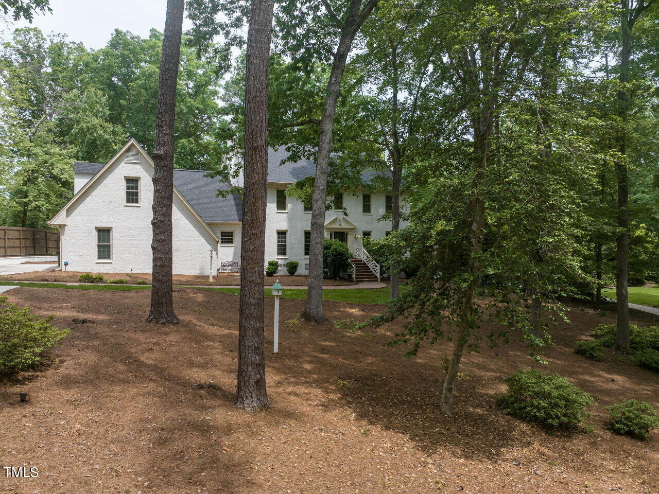 White brick house partly screened by mature trees, with steps leading to the rear entrance.