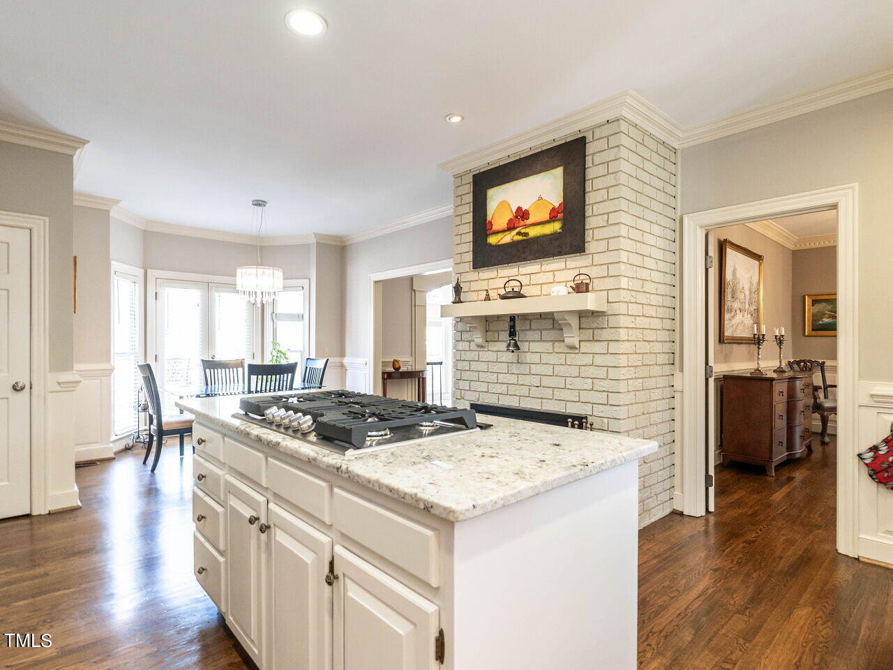Kitchen with a large gas cooktop island, white brick fireplace, and dining area by bright windows.