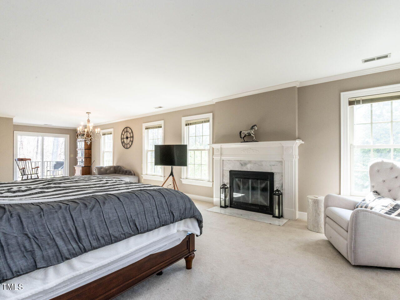 Spacious bedroom with a large bed, white fireplace, and bright windows overlooking a deck.