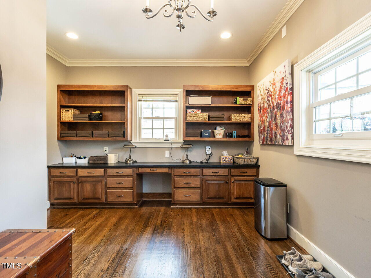 Home office with dark wood built-in desk and shelving, hardwood floors, and large windows.