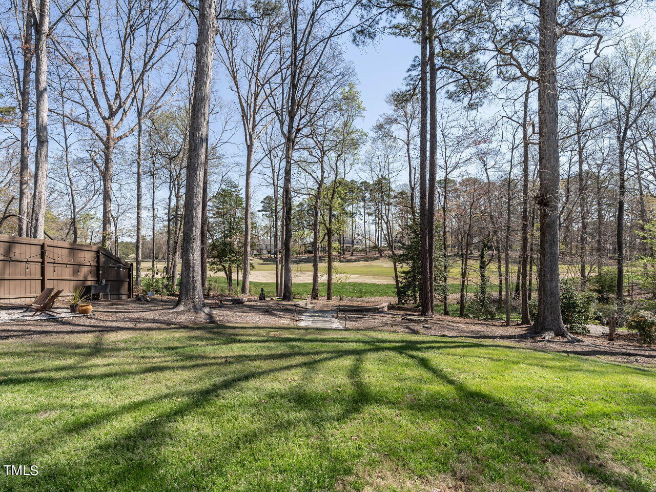 Wooded backyard with a green lawn and patio overlooking a golf course fairway.