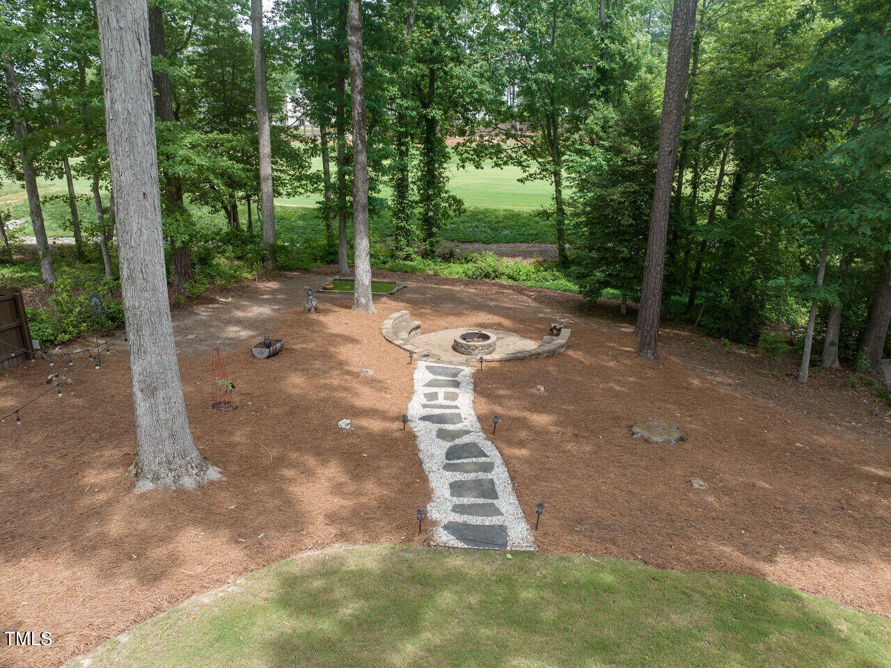 Wooded backyard with a curved stone fire pit area and a white gravel path.