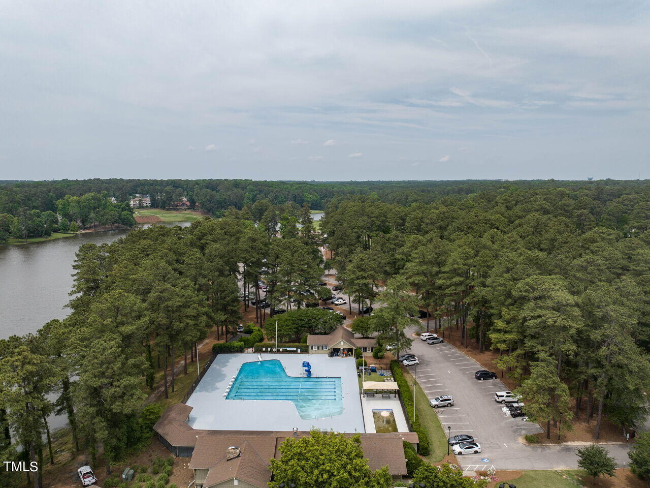 Aerial view of a community pool beside a lake, surrounded by trees and parking.