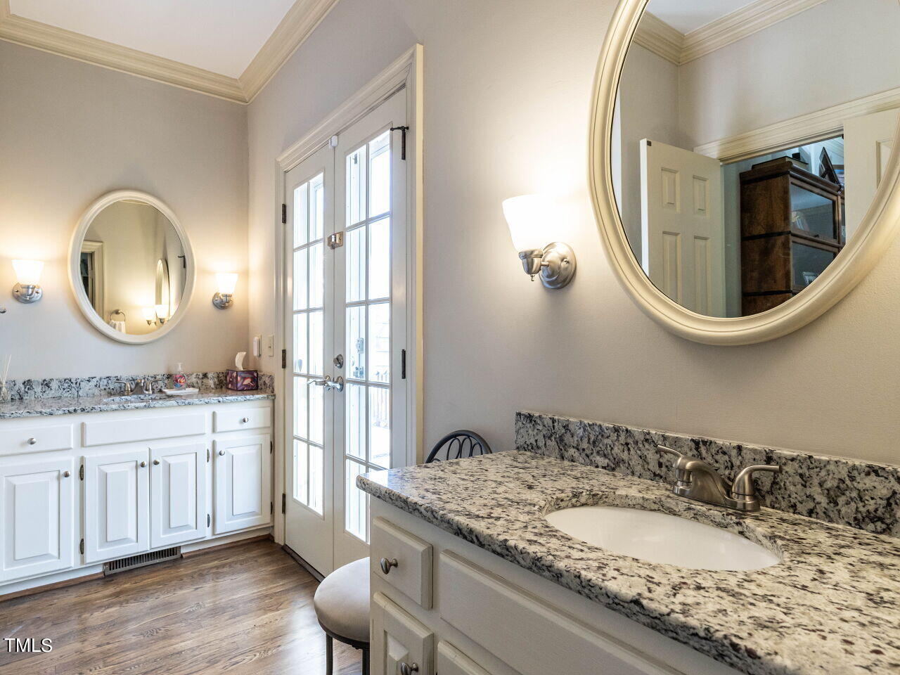 Bathroom with dual white vanities, speckled granite countertops, oval mirrors, and a glass-paneled door.