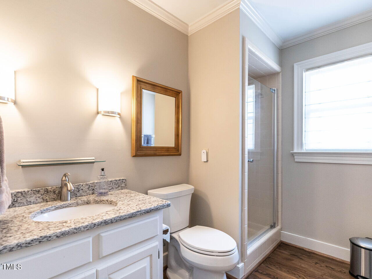 Bathroom with a granite vanity, framed mirror, and glass-enclosed shower beside a large window.