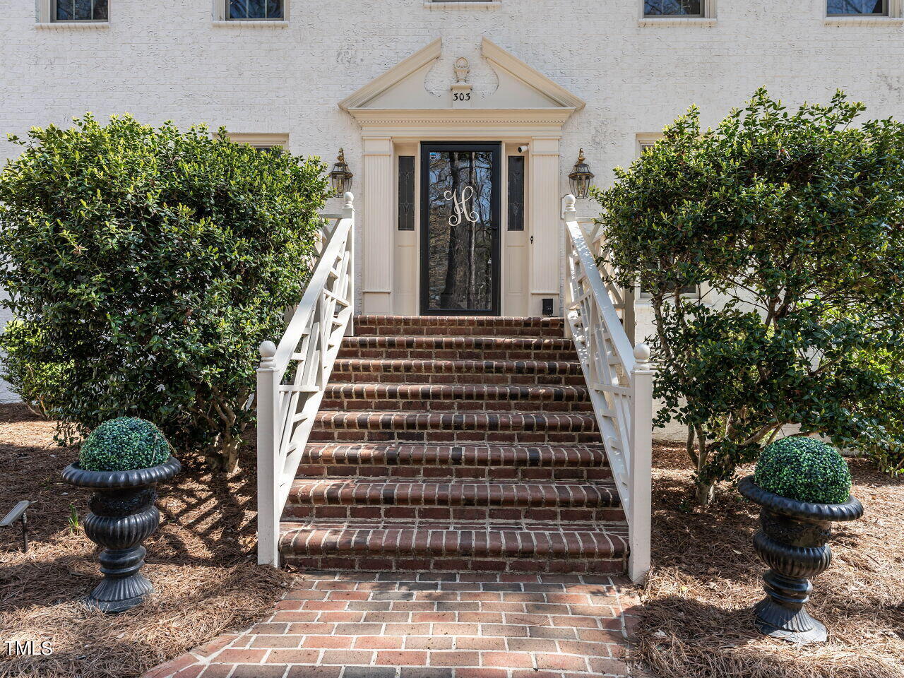 Home entrance with broad brick steps, white railings, and trimmed shrubs in urn planters.