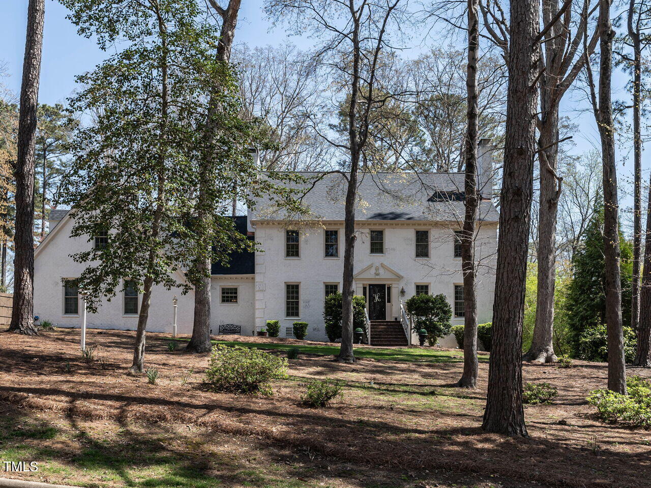 Two-story white house with a central entrance, framed by mature trees on a wooded lot.