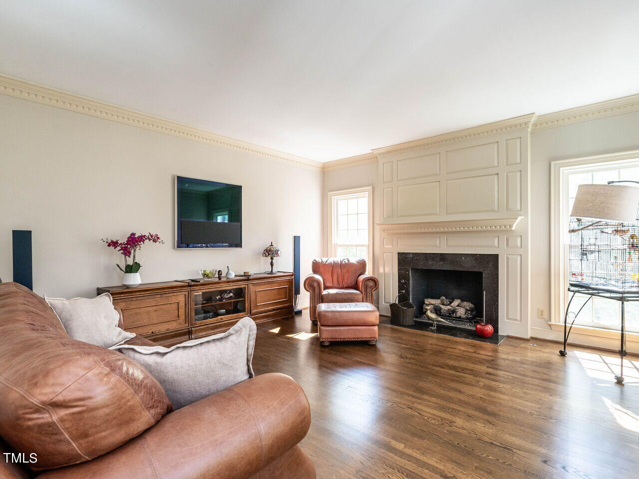 Living room with a paneled fireplace, leather seating, hardwood floors, and a wall-mounted television.