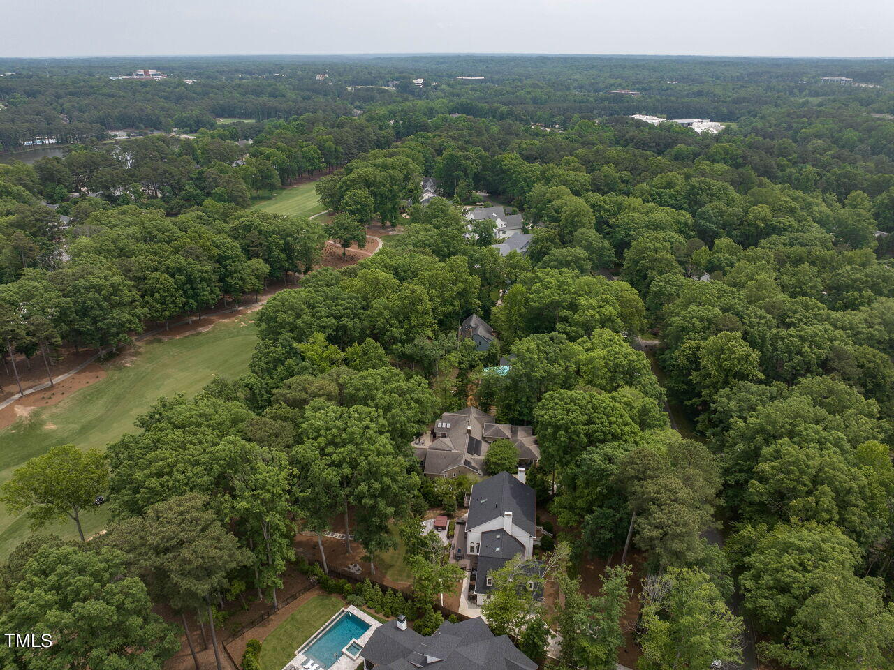 Aerial view of a wooded property with a backyard pool beside a golf course fairway.