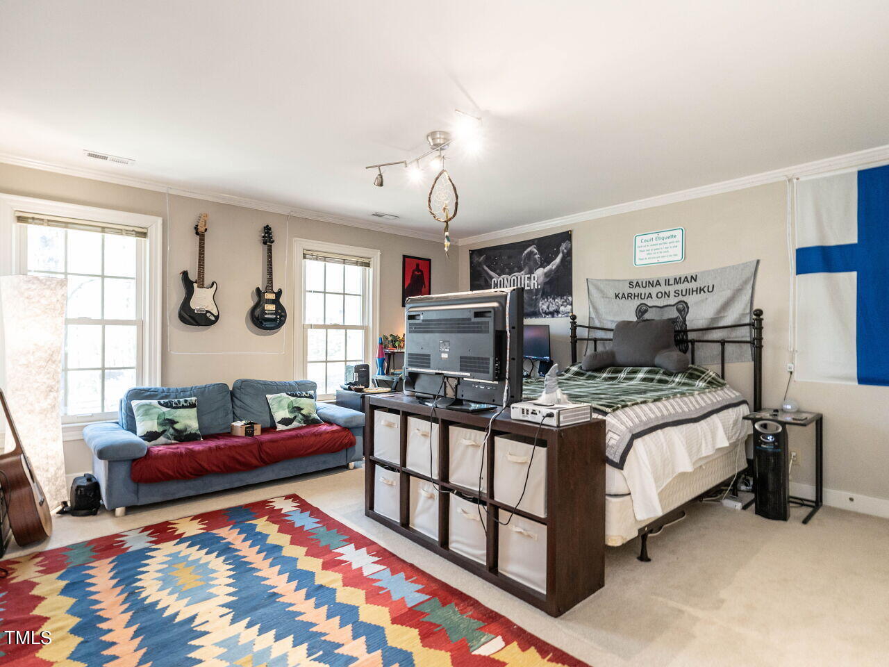 Bedroom with a bed, blue sofa, wall-mounted guitars, and colorful geometric rug.
