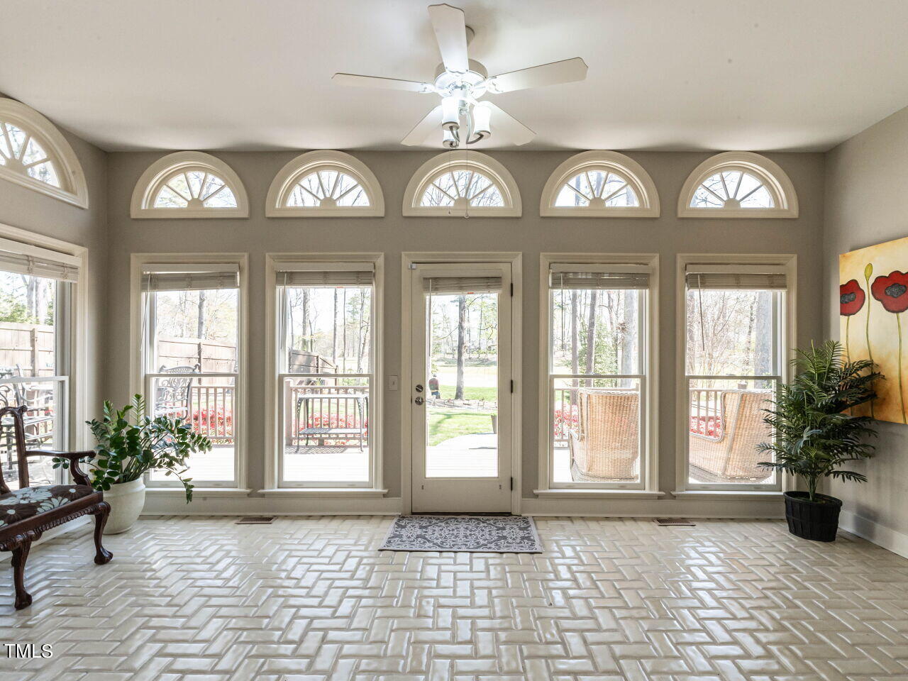 Sunroom with a tiled floor, ceiling fan, and tall windows overlooking a deck and yard.